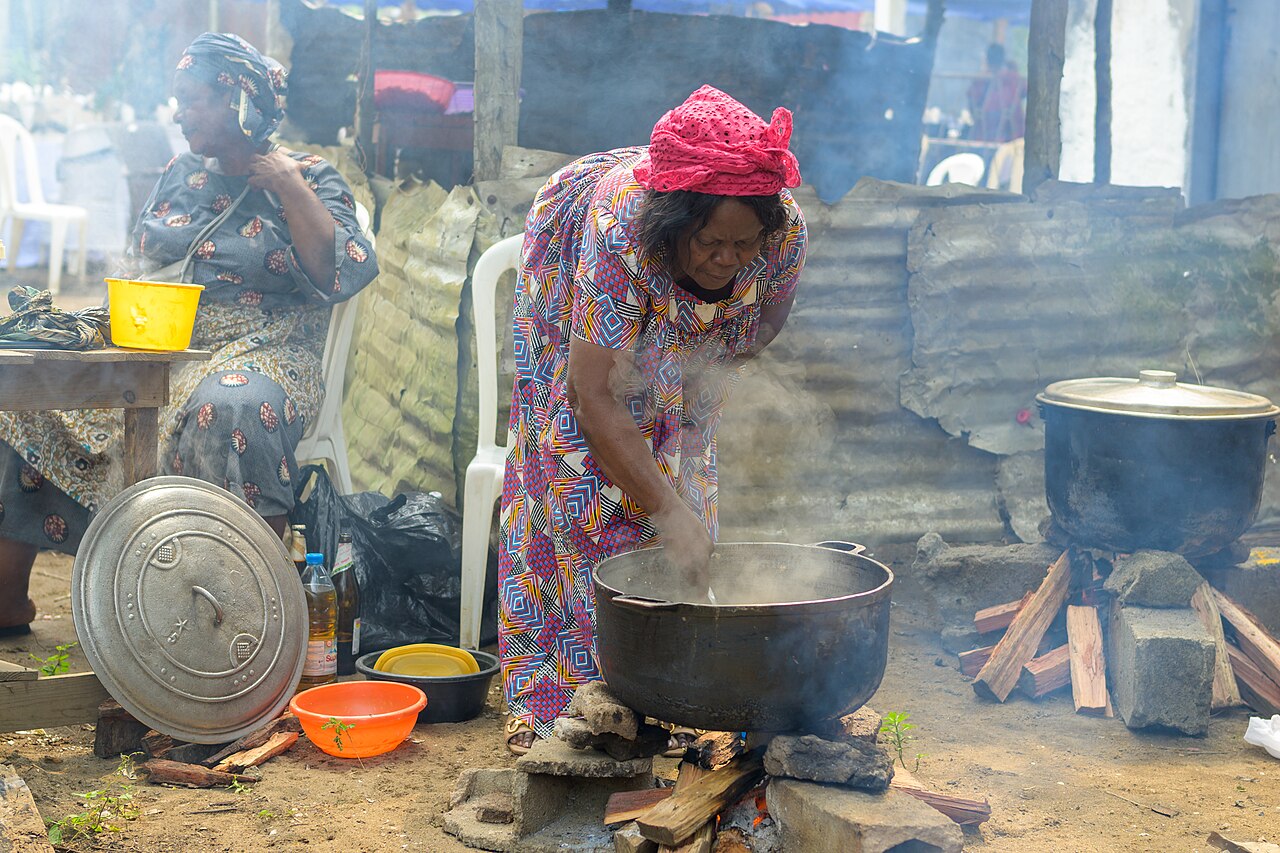A woman in a bright printed dress stirring a large pot over a wood fire